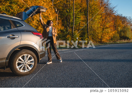 at sunset, a woman closes the trunk of a parked car at sunset, a woman closes the trunk of a parked car 105915092