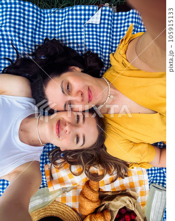 Two girls on a date lie on a blue blanket for a picnic in nature Two girls on a date lie on a blue blanket for a picnic in nature 105915133