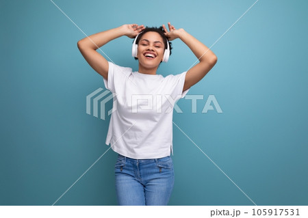 young brunette latin woman in a white t-shirt listens to her favorite music in bluetooth headphones young brunette latin woman in a white t-shirt listens to her favorite music in bluetooth headphones 105917531