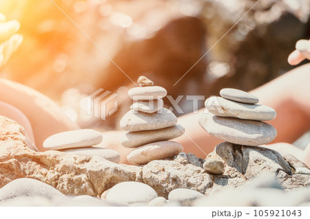 Woman with daughter bilds stones pyramid on seashore on a sunny day on the blue sea background. Happy family holidays. Pebble beach, calm sea. Concept of happy vacation on the sea, meditation, spa Woman with daughter bilds stones pyramid on seashore on a sunny day on the blue sea background. Happy family holidays. Pebble beach, calm sea. Concept of happy vacation on the sea, meditation, spa 105921043