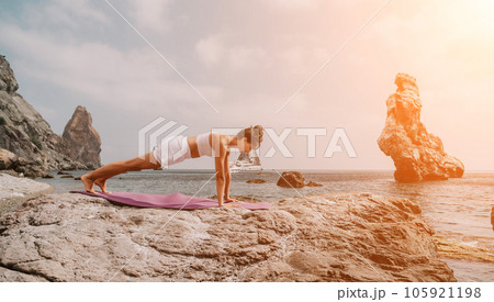 Fitness woman sea. A happy middle aged woman in white sportswear exercises morning outdoors on a beach with volcanic rocks by the sea. Female fitness pilates yoga routine concept. Healthy lifestyle. Fitness woman sea. A happy middle aged woman in white sportswear exercises morning outdoors on a beach with volcanic rocks by the sea. Female fitness pilates yoga routine concept. Healthy lifestyle. 105921198