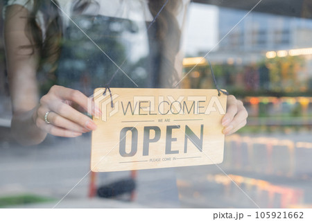 Female store owner turning open sign board of start up coffee shop cafe and restaurant through the door glass and opening the daily service 105921662