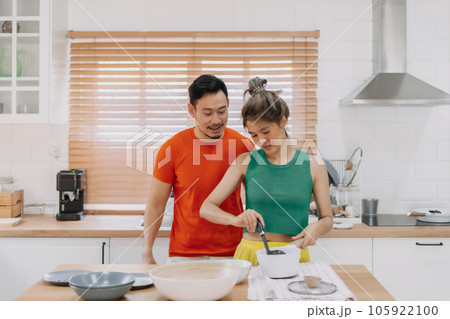 Husband looking at wife who cooking lunch for him. Happy couple in kitchen. 105922100