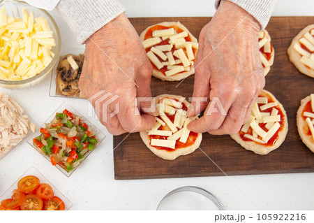 Adding toppings to the mini pizzas. Adding cheese. Delicious homemade mini pizzas preparation. Adding toppings to the mini pizzas. Adding cheese. Delicious homemade mini pizzas preparation. 105922216