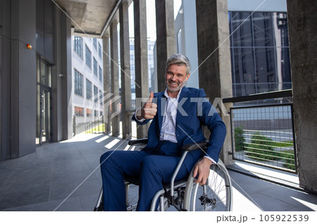Disabled man wearing official style suit in wheelchair showing thumb up like gesture. 105922539