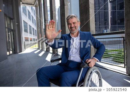 Gray haired disabled man wearing official style suit in wheelchair, raising palm, giving high five 105922540