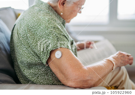 Diabetic senior patient using continuous glucose monitor to check blood sugar level at home. 105922960