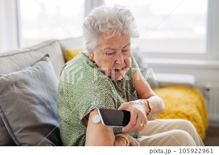 Diabetic senior patient checking blood glucose level at home using continuous glucose monitor. 105922961