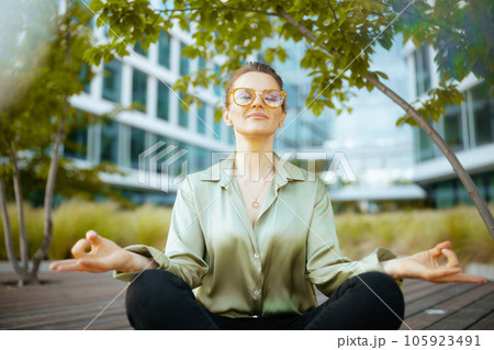relaxed woman worker in green blouse and eyeglasses meditating 105923491