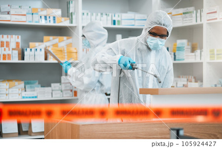 Biohazard, spray and disinfect with people in a pharmacy for decontamination after a medical accident. Hazmat, chemical or cleaning with healthcare personnel in a drugstore to sanitize and isolate Biohazard, spray and disinfect with people in a pharmacy for decontamination after a medical accident. Hazmat, chemical or cleaning with healthcare personnel in a drugstore to sanitize and isolate 105924427