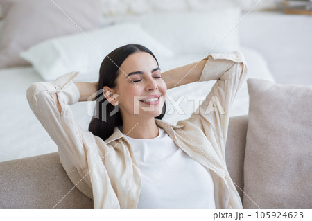 Beautiful young smiling woman relaxing on sofa at home, sitting relaxed with eyes closed and hands behind head. Beautiful young smiling woman relaxing on sofa at home, sitting relaxed with eyes closed and hands behind head. 105924623