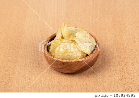 Thin potato chips in a bowl over a wooden background. 105924995