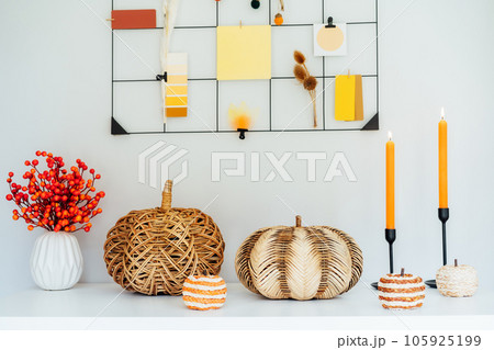 Cozy autumn home interior decor- various decorative wicker pumpkins, candles, seasonal flowers in vase on the white table with mood board with fall colors palette notes on the wall. Mood inspiration. 105925199