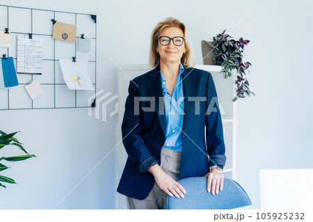 Confident middle aged businesswoman standing near grid mood board with pinned plan in office workspace. Portrait of experienced senior female professional, business coach team leader in modern office 105925232