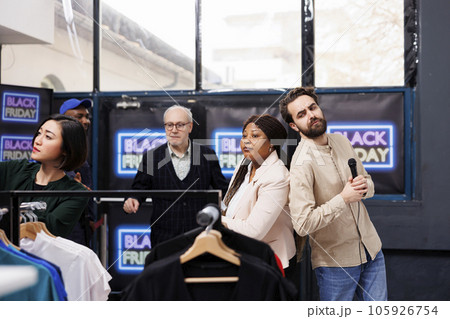 Shoppers browsing among clothing on Black Friday, people looking for bargains. Clothes store workers hosting annual retail sale event, welcoming greeting customers in modern fashion outlet 105926754