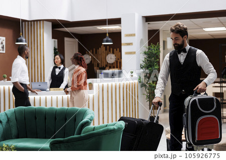 Hotel bellboy carrying bags for guests, helping tourists to find room after doing check in procedure. Male employee acting as concierge, providing luxury service for people with luggage. 105926775