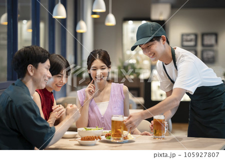 ビールのジョッキを運ぶホールスタッフとテーブル席の若い男女のグループ　 105927807