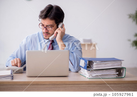 Young male employee talking by phone at workplace Young male employee talking by phone at workplace 105927961
