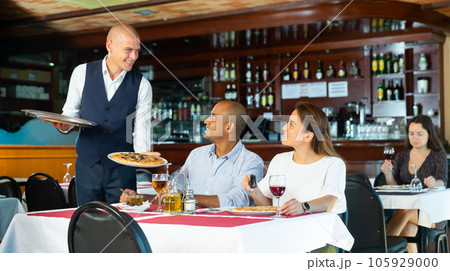 Polite waiter serving pizza to hispanic couple in restaurant 105929000