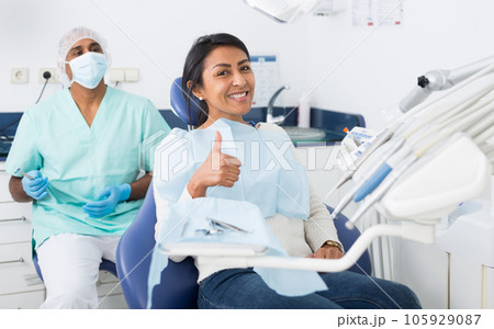 Woman sitting in dental chair after teeth cure giving thumb up 105929087