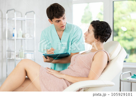 Young male doctor signing papers while talking with woman patient 105929101