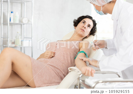 Middle-aged woman having vein injection lying on clinical chair Middle-aged woman having vein injection lying on clinical chair 105929155