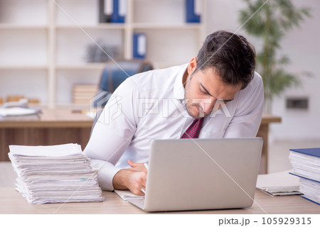 Young male employee and too much work at workplace 105929315