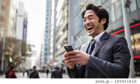都会・ビジネス街でスマホを見て喜ぶ笑顔のアジア人ビジネスマン 都会・ビジネス街でスマホを見て喜ぶ笑顔のアジア人ビジネスマン 105931610