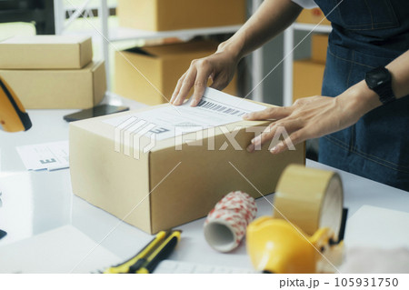 Young business owner putting shipping label on parcel.. Young business owner putting shipping label on parcel.. 105931750