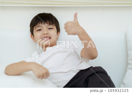 Happy cheerful Asian little young boy sits on the sofa and plays with camera, a little boy looking and smiling to camera. 105932125
