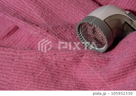 Anti-pilling razor. Device for shaving clothes. Anti-Plush fabric Shaver. Electric portable sweater pill defuzzer Lint remover from pink acrylic or wool sweater. Electric device fabric shaver after 105932330