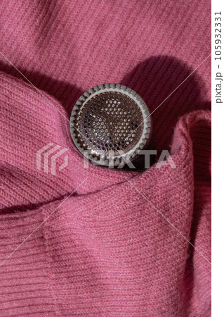 Anti-pilling razor. Device for shaving clothes. Anti-Plush fabric Shaver. Electric portable sweater pill defuzzer Lint remover from pink acrylic or wool sweater. Electric device fabric shaver after Anti-pilling razor. Device for shaving clothes. Anti-Plush fabric Shaver. Electric portable sweater pill defuzzer Lint remover from pink acrylic or wool sweater. Electric device fabric shaver after 105932331
