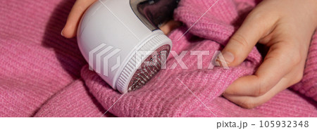 Woman using Anti-pilling razor at home. Device for shaving clothes. Anti-Plush fabric Shaver. Electric portable sweater pill defuzzer Lint remover from pink acrylic or wool sweater. Slow fashion Woman using Anti-pilling razor at home. Device for shaving clothes. Anti-Plush fabric Shaver. Electric portable sweater pill defuzzer Lint remover from pink acrylic or wool sweater. Slow fashion 105932348