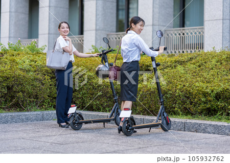 オフィス街で電動キックボードに乗って移動する若い女性社会人イメージ｜電動キックボードイメージ 105932762
