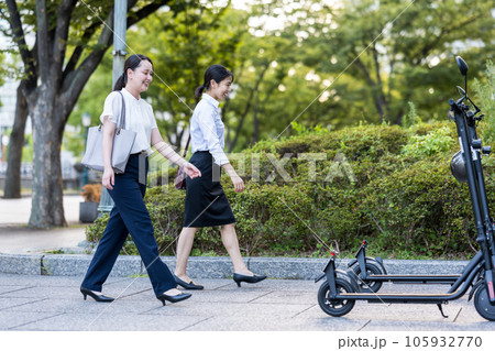 オフィス街で電動キックボードに乗って移動する若い女性社会人イメージ｜電動キックボードイメージ 105932770