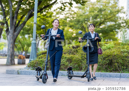 オフィス街で電動キックボードに乗って移動する若い女性社会人イメージ｜電動キックボードイメージ 105932786