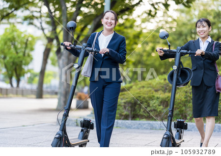 オフィス街で電動キックボードに乗って移動する若い女性社会人イメージ｜電動キックボードイメージ 105932789