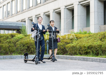 オフィス街で電動キックボードに乗って移動する若い女性社会人イメージ｜電動キックボードイメージ 105932795