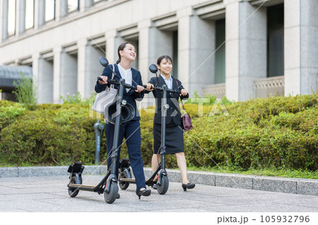 オフィス街で電動キックボードに乗って移動する若い女性社会人イメージ｜電動キックボードイメージ 105932796