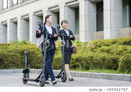 オフィス街で電動キックボードに乗って移動する若い女性社会人イメージ｜電動キックボードイメージ 105932797