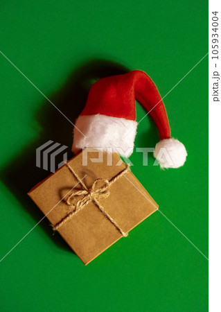 Santa hat on paper gift box present on green background. Copy space for your text. Mock up for advertisement. Holiday Christmas composition Santa hat on paper gift box present on green background. Copy space for your text. Mock up for advertisement. Holiday Christmas composition 105934004
