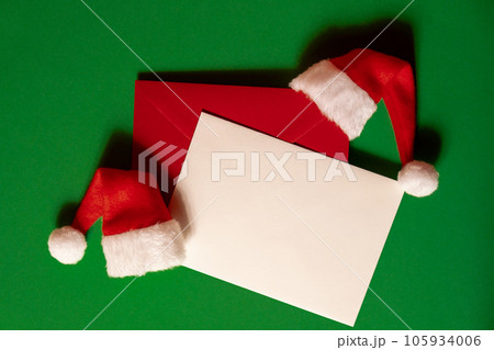 Santa hat with empty paper card note envelope on green background. Copy space for your text. Mock up for advertisement. Holiday Christmas composition 105934006