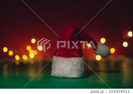 Santa hat on isometric green red background. Defocused lights on backdrop Copy space for your text. Mock up for advertisement. Holiday Christmas composition. Minimalistic greeting card Santa hat on isometric green red background. Defocused lights on backdrop Copy space for your text. Mock up for advertisement. Holiday Christmas composition. Minimalistic greeting card 105934053