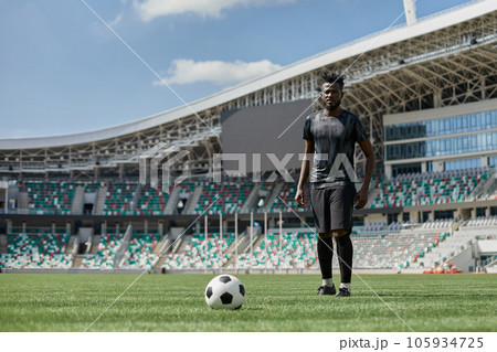Professional male football, soccer player on stadium background. African fit athlete practicing, playing excited 105934725