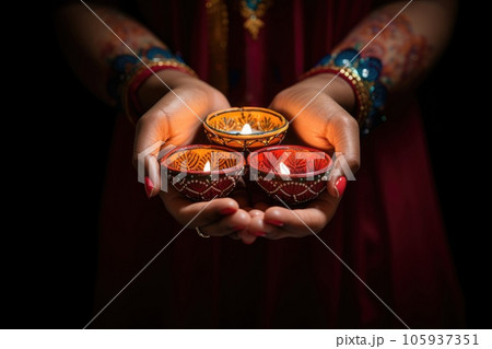 Woman hands with henna holding colorful clay diya lamps lit during diwali celebration Woman hands with henna holding colorful clay diya lamps lit during diwali celebration 105937351