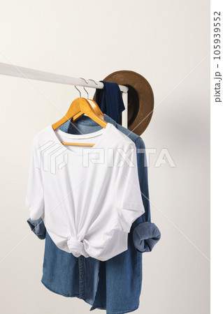 White t shirt, hat and denim shirt hanging from clothes rail with copy space on white background 105939552