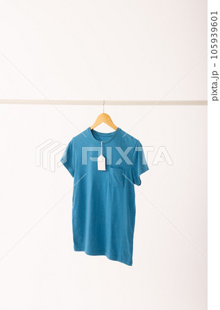 Blue t shirt with tag on hanger hanging from clothes rail with copy space on white background Blue t shirt with tag on hanger hanging from clothes rail with copy space on white background 105939601