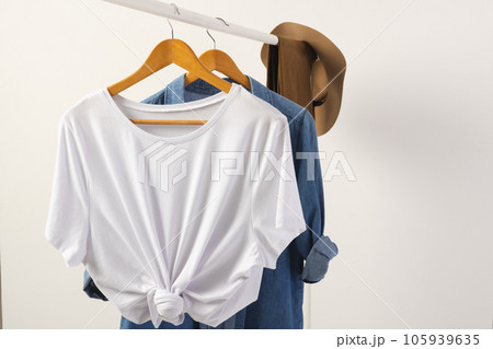 White t shirt, hat and denim shirt hanging from clothes rail with copy space on white background 105939635