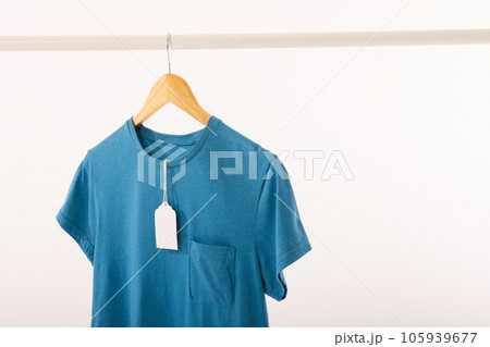 Blue t shirt with tag on hanger hanging from clothes rail with copy space on white background Blue t shirt with tag on hanger hanging from clothes rail with copy space on white background 105939677