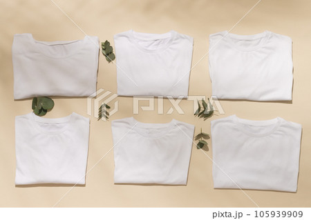 Close up of folded white t shirts with leaves and copy space on yellow background Close up of folded white t shirts with leaves and copy space on yellow background 105939909